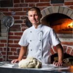 Chief chef kneads the dough on table with flour for cooking Italian pizza near a wood-burning oven in the kitchen